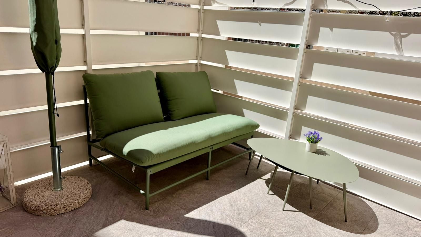 Une pièce avec un canapé vert, une petite table sur laquelle est posée une plante en pot et un lampadaire.