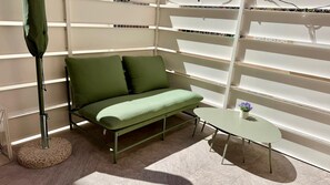 Um quarto com um sofá verde, uma mesa pequena com uma planta em vaso e um abajur.