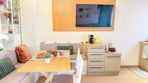 Uma sala de estar moderna com sofá, mesa de jantar, estação de café e TV na parede.
