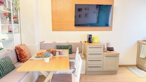 Een moderne woonkamer met een bank, eettafel, koffiehoek en een aan de muur bevestigde televisie.