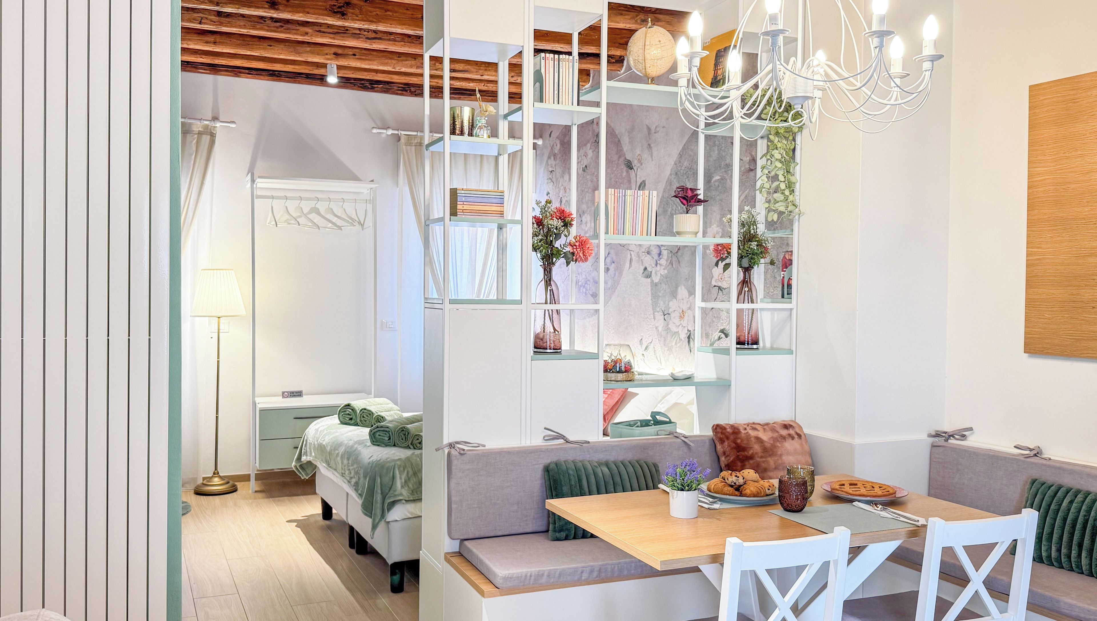 Quarto moderno com teto de madeira, área de jantar com mesa e cadeiras, sofá e estante com diversos objetos.