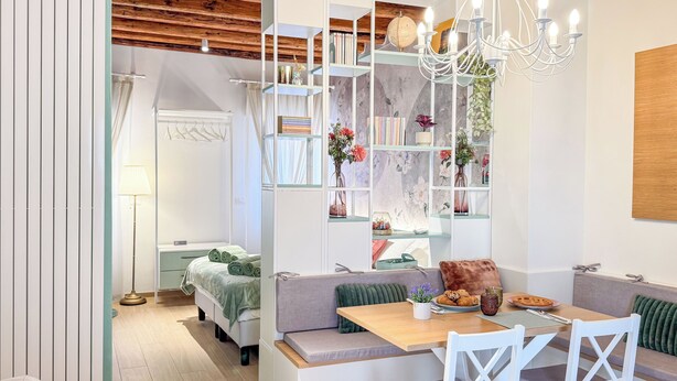 Quarto moderno com teto de madeira, área de jantar com mesa e cadeiras, sofá e estante com diversos objetos.