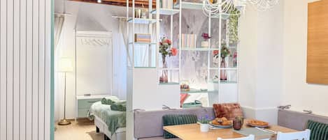 A modern room with a wooden ceiling, a dining area with a table and chairs, a sofa, and a bookshelf with various items.