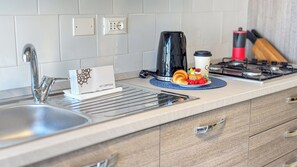 Una cuina moderna amb un vàter d'acer inoxidable, una cafetera, un croissant i un plat de fruita.