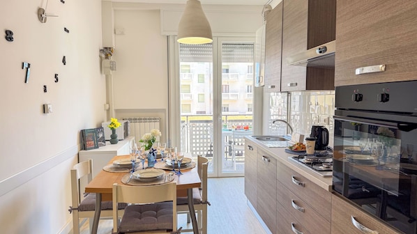 Uma cozinha compacta com eletrodomésticos modernos, uma área de refeições com mesa posta para dois e vista para a varanda.