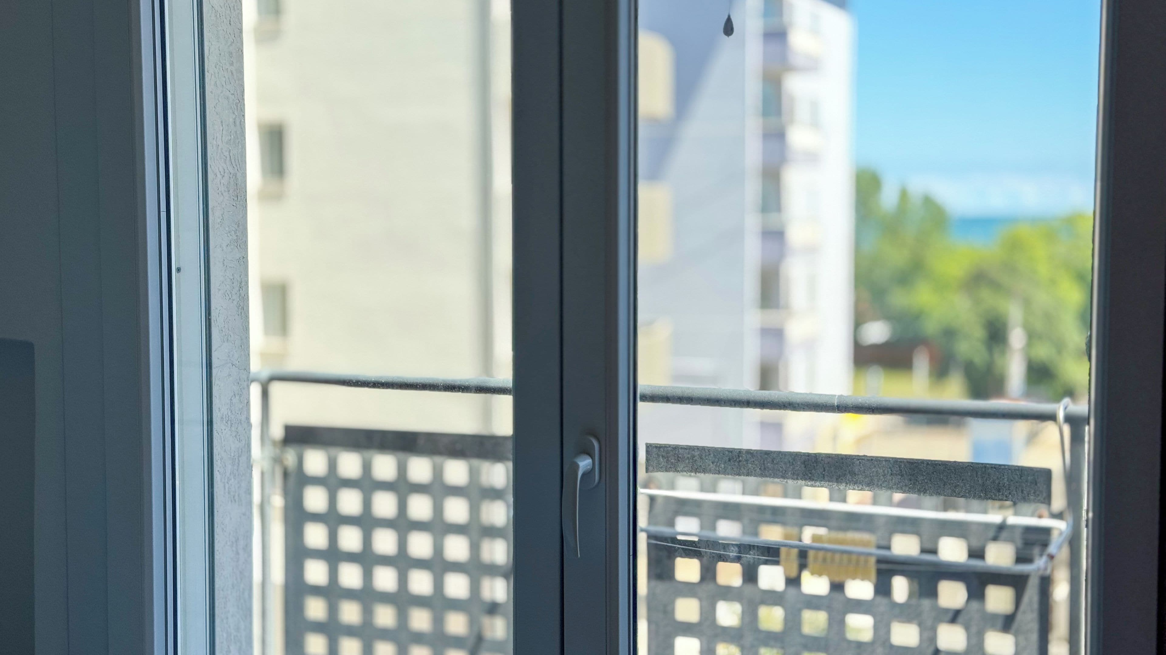 Ein Fenster mit einem Metallbalkongeländer und Blick auf ein Gebäude, bewölkter Himmel.