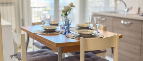 A dining table set with plates, glasses, and a vase with flowers. There are cushioned chairs around the table.