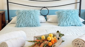 Cama bem arrumada com travesseiros macios, um buquê de flores e toalhas dobradas.
