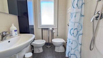Baño con lavamanos, dos inodoros, una ventana y cortina de ducha.