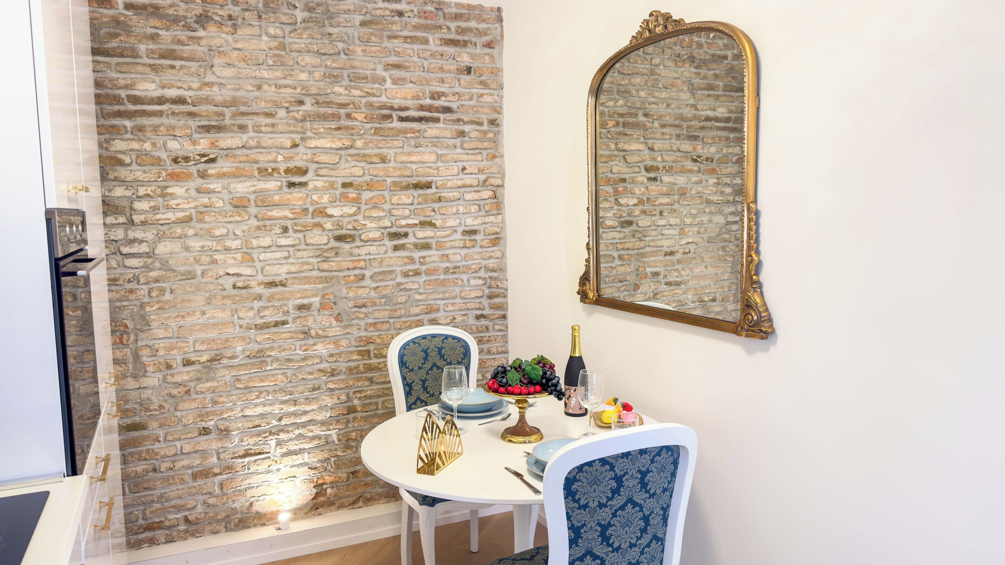 A dining area with a brick wall, a mirror, and a table set with plates, glasses, and a fruit bowl.