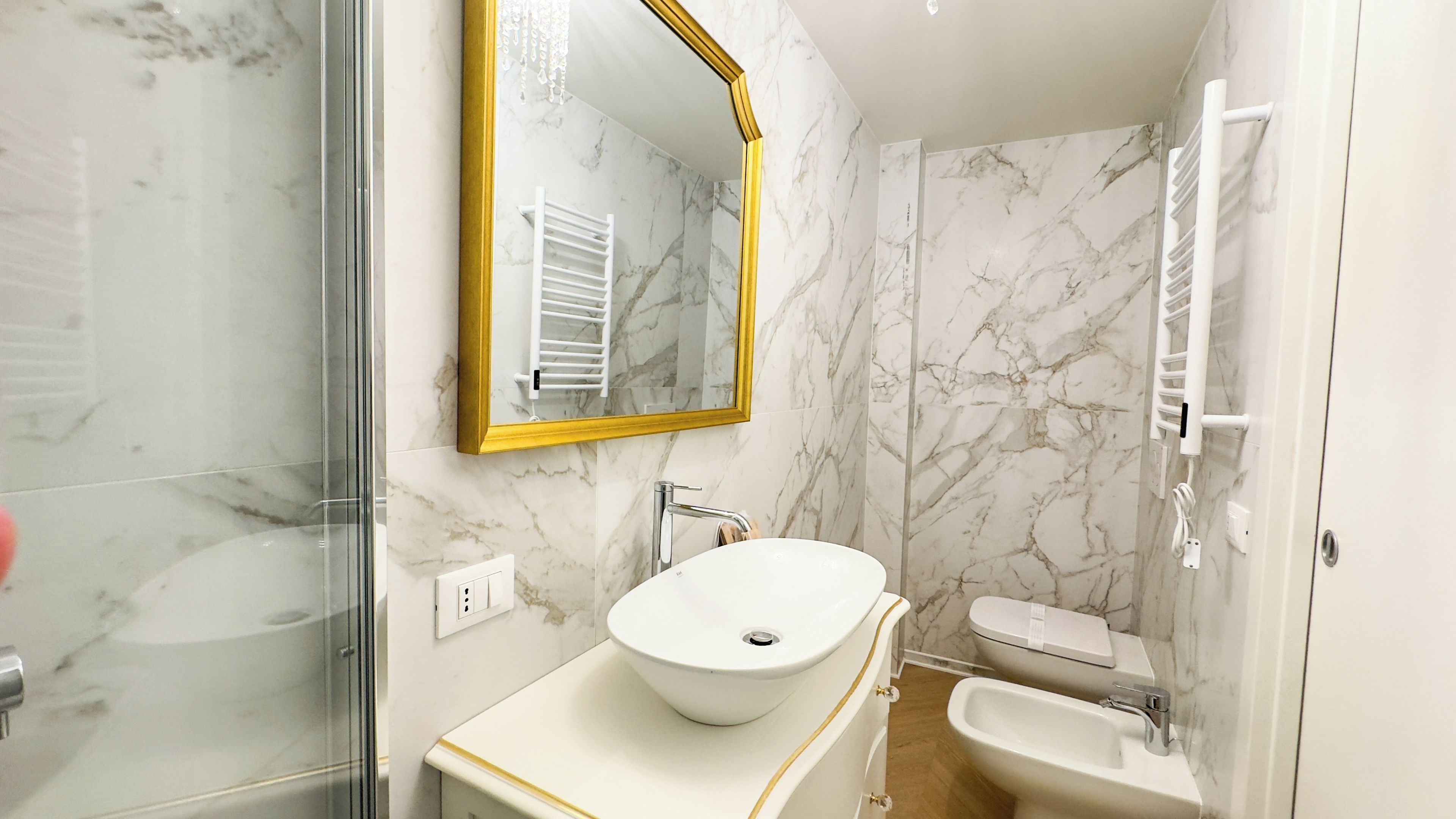 Et badeværelse med en hvid vask, et spejl med gylden ramme, et toilet og en bruseniche.