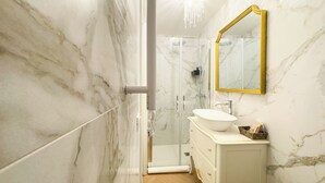 A bathroom with a marble wall, a white sink, a gold-framed mirror, and a shower enclosure. - Suite Palazzo Ravagnan by Ca-sa Check (Chioggia)