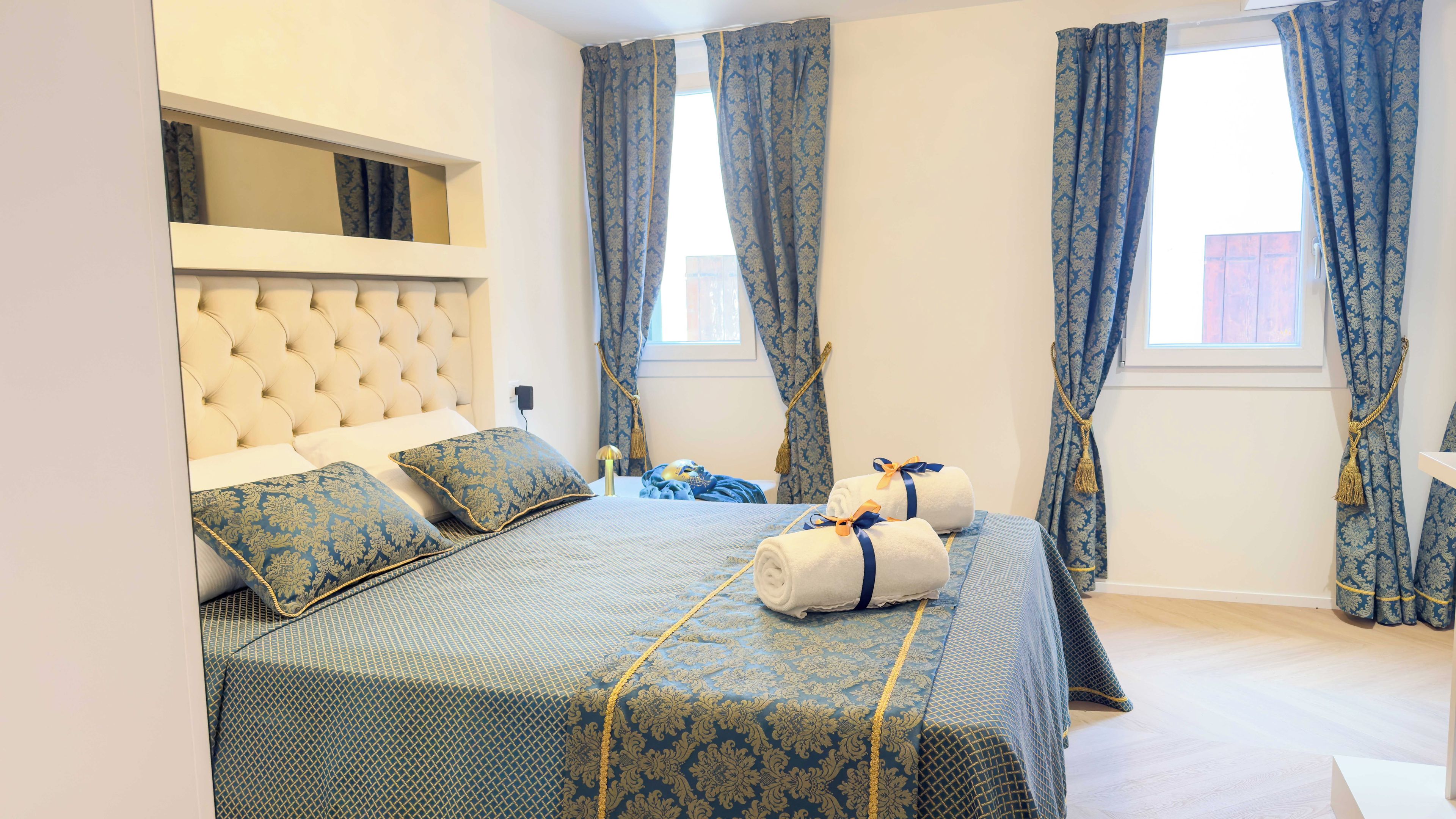 Une chambre à coucher avec une tête de lit capitonnée, un lit recouvert d’une literie à motifs et des rideaux bleus agrémentés de glands.