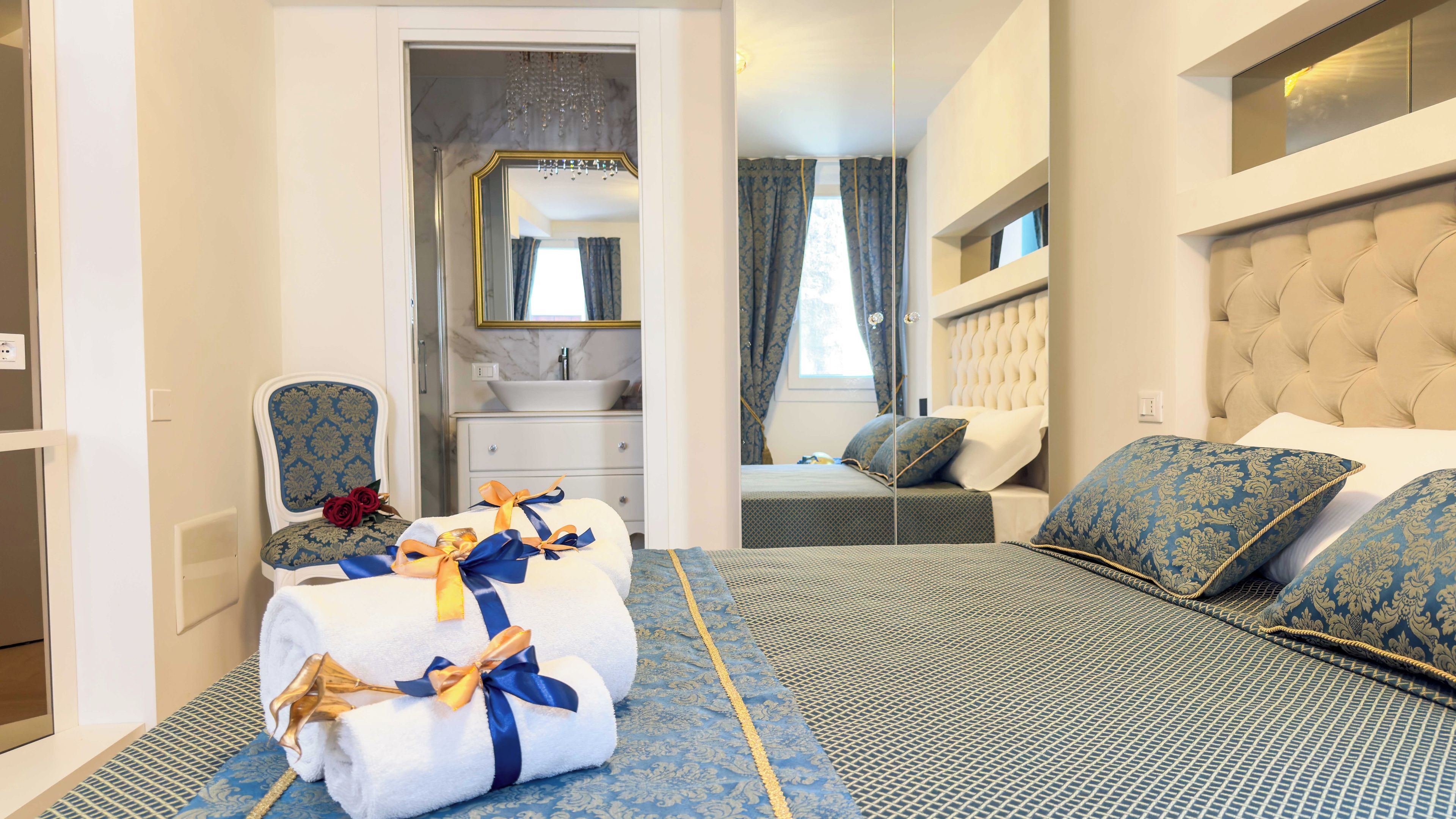 A hotel room with a bed, a chair, a vanity with a mirror, and a window with curtains.