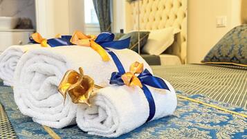 A neatly rolled white towel with gold and blue ribbons, placed on a patterned blue carpet in a hotel room.