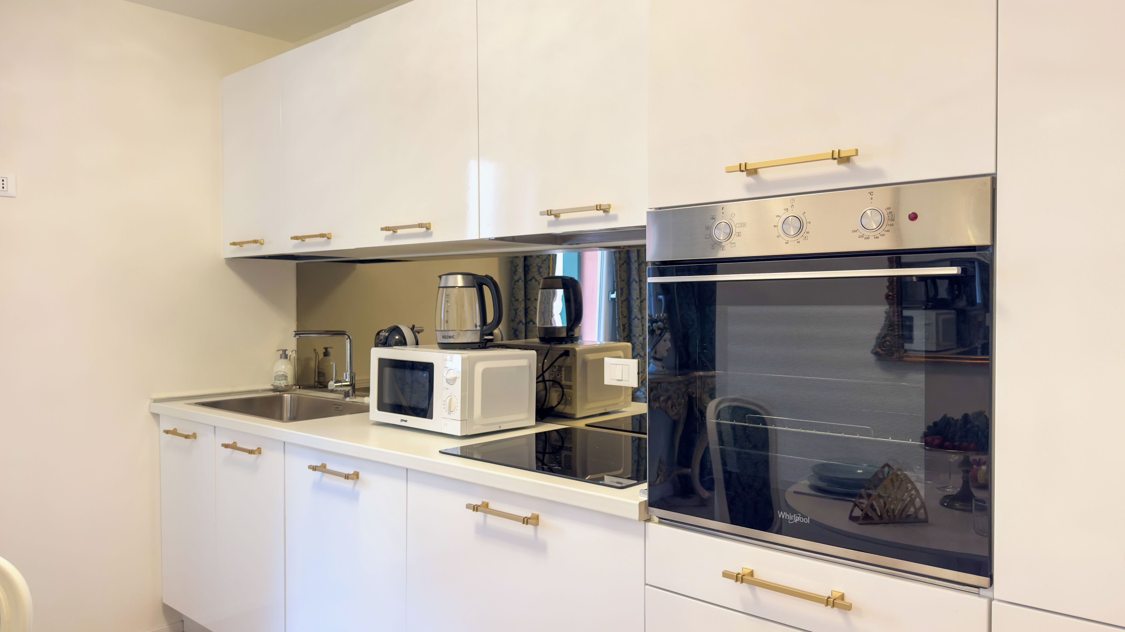 A compact kitchen with white cabinets, a built-in microwave, a coffee maker, and an oven.