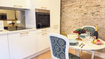 A modern kitchen with white cabinets, a built-in oven, and a dining area with a brick wall backdrop.