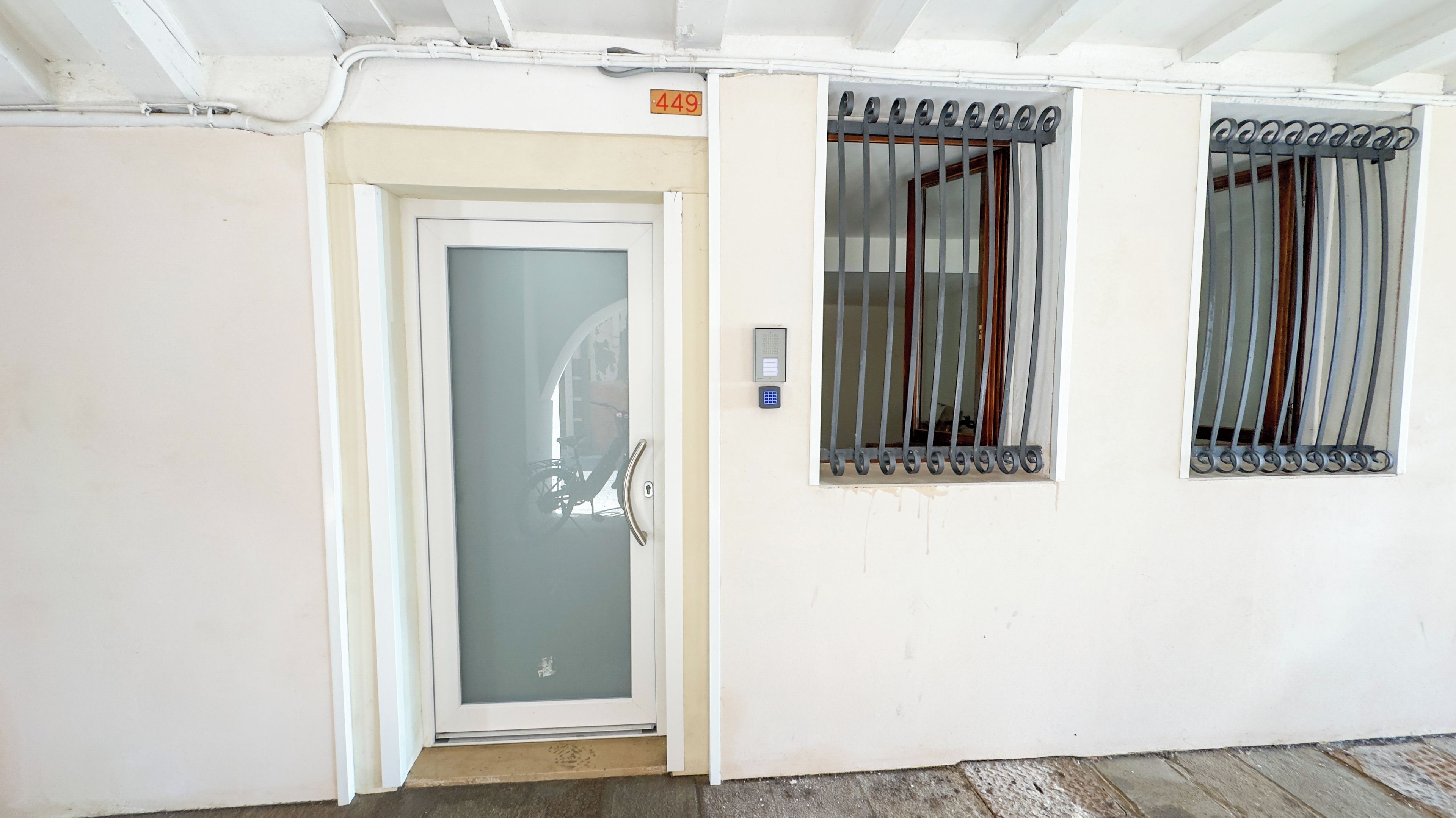 A white building with a numbered door, a bicycle outside, and a window with metal bars.