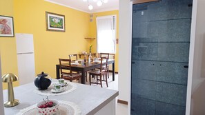 A dining area with a table set for four, chairs, a white refrigerator, and a framed picture on the wall. - Dimora Euganea by Ca-sa Check (Monselice)