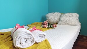Una cama con toallas blancas enrolladas, una colcha amarilla, rosas rosadas y almohadas blancas mullidas frente a una pared verde azulado.