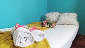 A bed with rolled white towels, a yellow blanket, pink roses, and fluffy white pillows against a teal wall. - Dimora Euganea by Ca-sa Check (Monselice)