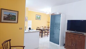 Una sala de estar con televisor, un mueble de madera y un comedor con sillas y una mesa.