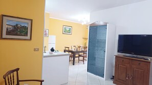 A living room with a TV, wooden cabinet, and dining area with chairs and a table. - Dimora Euganea by Ca-sa Check (Monselice)