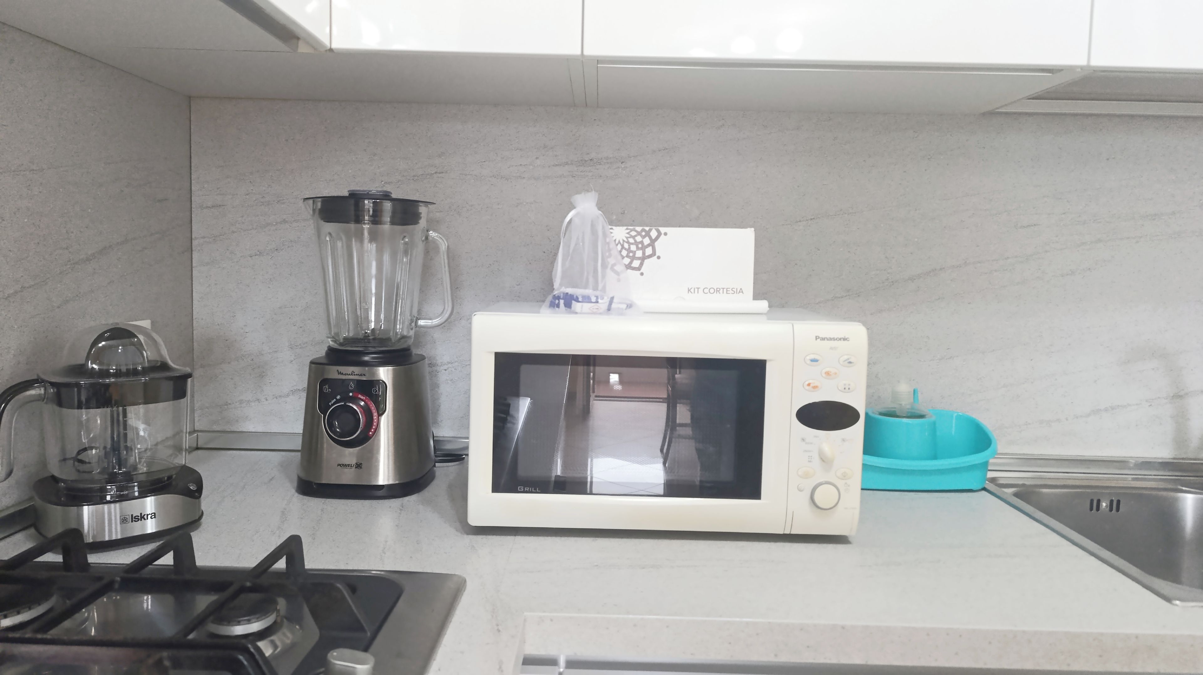 A kitchen with a gas stove, a blender, a microwave, and a kettle.