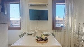 A dining area with a table set for two, a flat-screen TV mounted on the wall, and a window with curtains. - Mi Casa Es Tu Casa by Ca-sa Check (Chioggia)