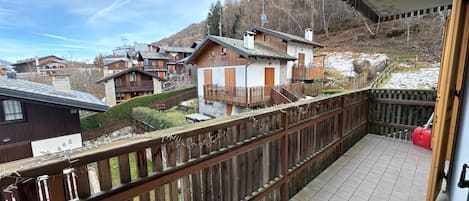 A balcony with a wooden railing overlooking a residential area with houses and a mountain backdrop.