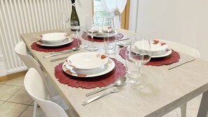 Mesa de jantar posta com pratos, talheres e copos de vinho, com uma garrafa de vinho e um tapete decorativo.