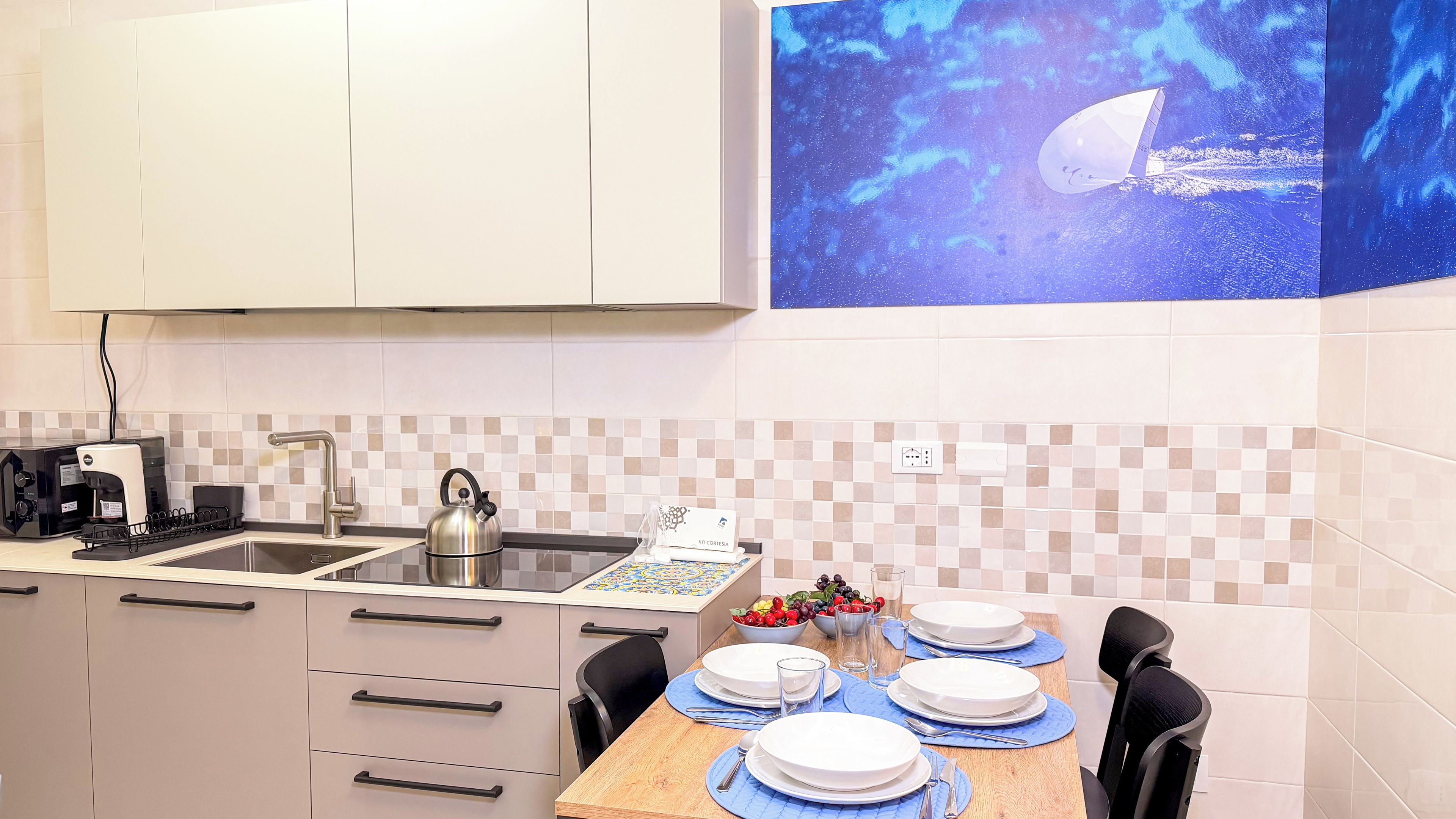 Cocina moderna con hervidor, cafetera y comedor preparado para cuatro personas, con platos y cubiertos.