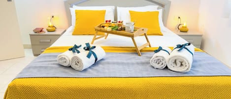 A neatly made bed with towels, a tray of fruit, and a cup on a bedside table.