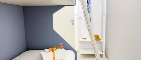 A bunk bed with a towel and flowers, a white shelf with a hat and sunglasses, and a white ladder.