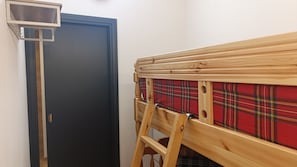 Una habitación con una puerta oscura, un banco de madera con cojín de cuadros y un estante pequeño encima.