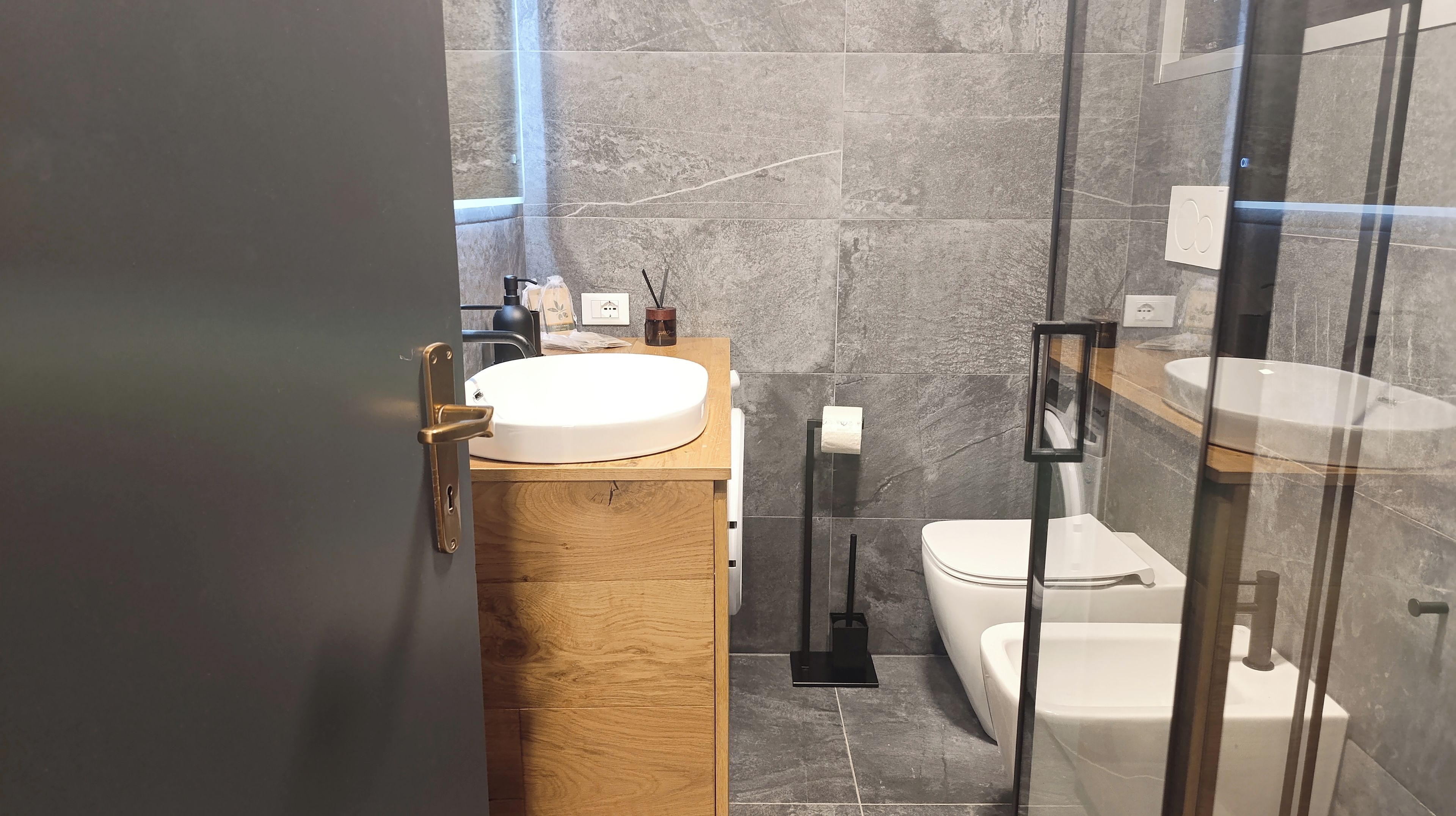 A modern bathroom with a wooden vanity, a white sink, a toilet, and a glass shower enclosure.
