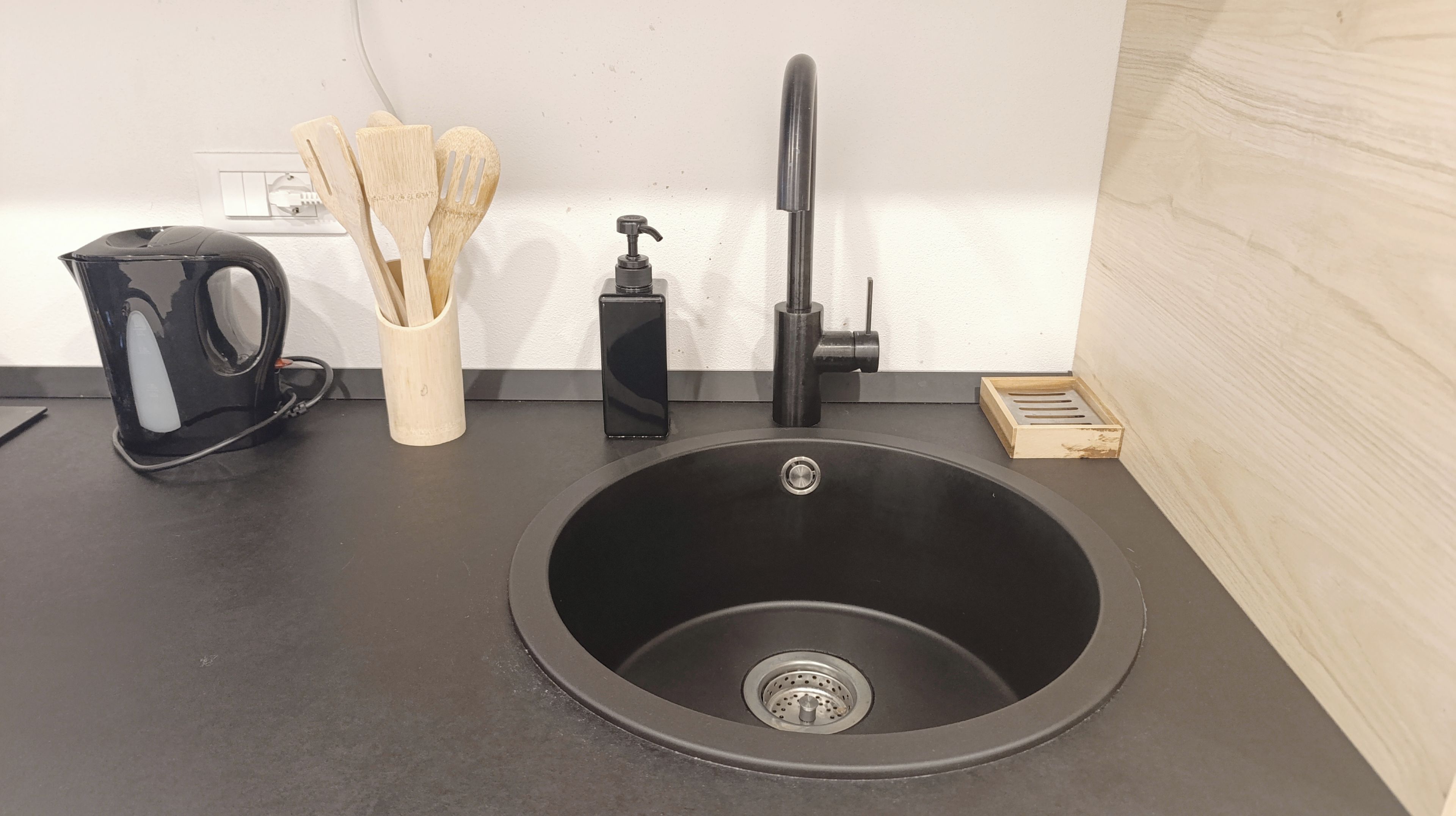 A kitchen sink with a faucet, a coffee maker, and a container with wooden utensils.