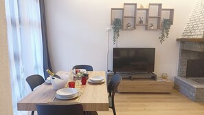 Uma área de refeições com uma mesa de madeira posta para dois, uma televisão e uma lareira.