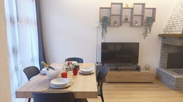 Uma área de refeições com uma mesa de madeira posta para dois, uma televisão e uma lareira.