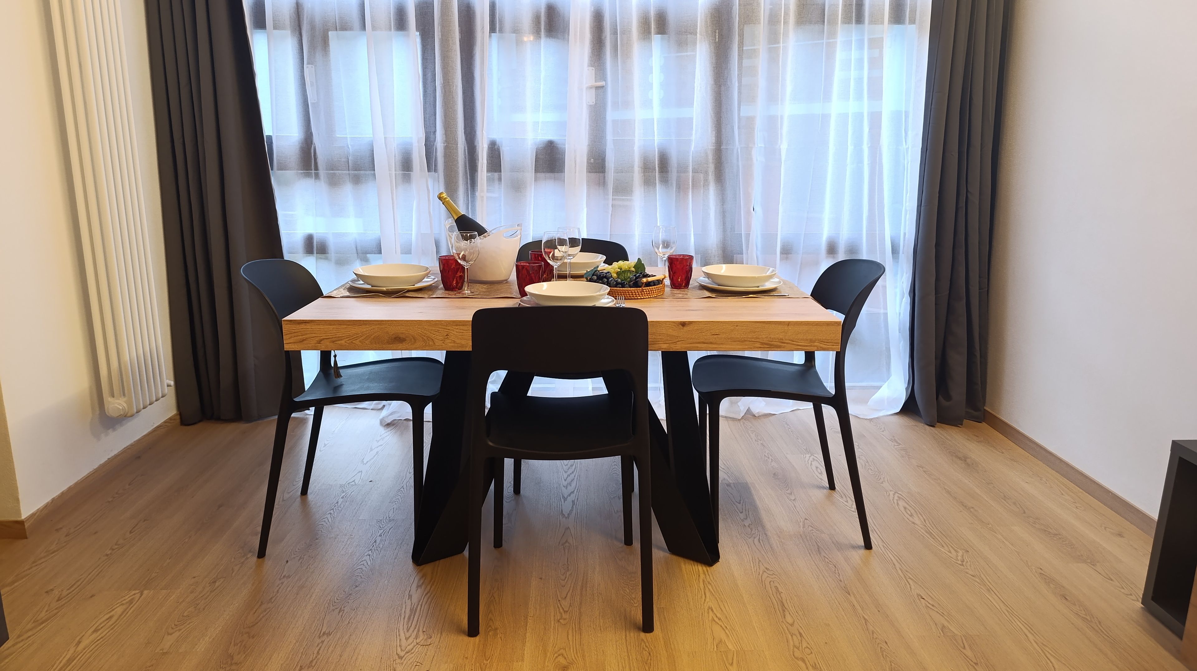 A dining area with a wooden table, black chairs, and a window with sheer curtains.