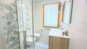 A bathroom with a glass shower enclosure, a toilet, a sink, and a mirror.