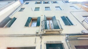 Un edificio con varias ventanas, algunas con persianas, y un balcón visible con barandilla de metal.