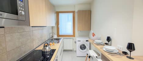 A modern kitchen with a microwave, stove, washing machine, and a window providing natural light.