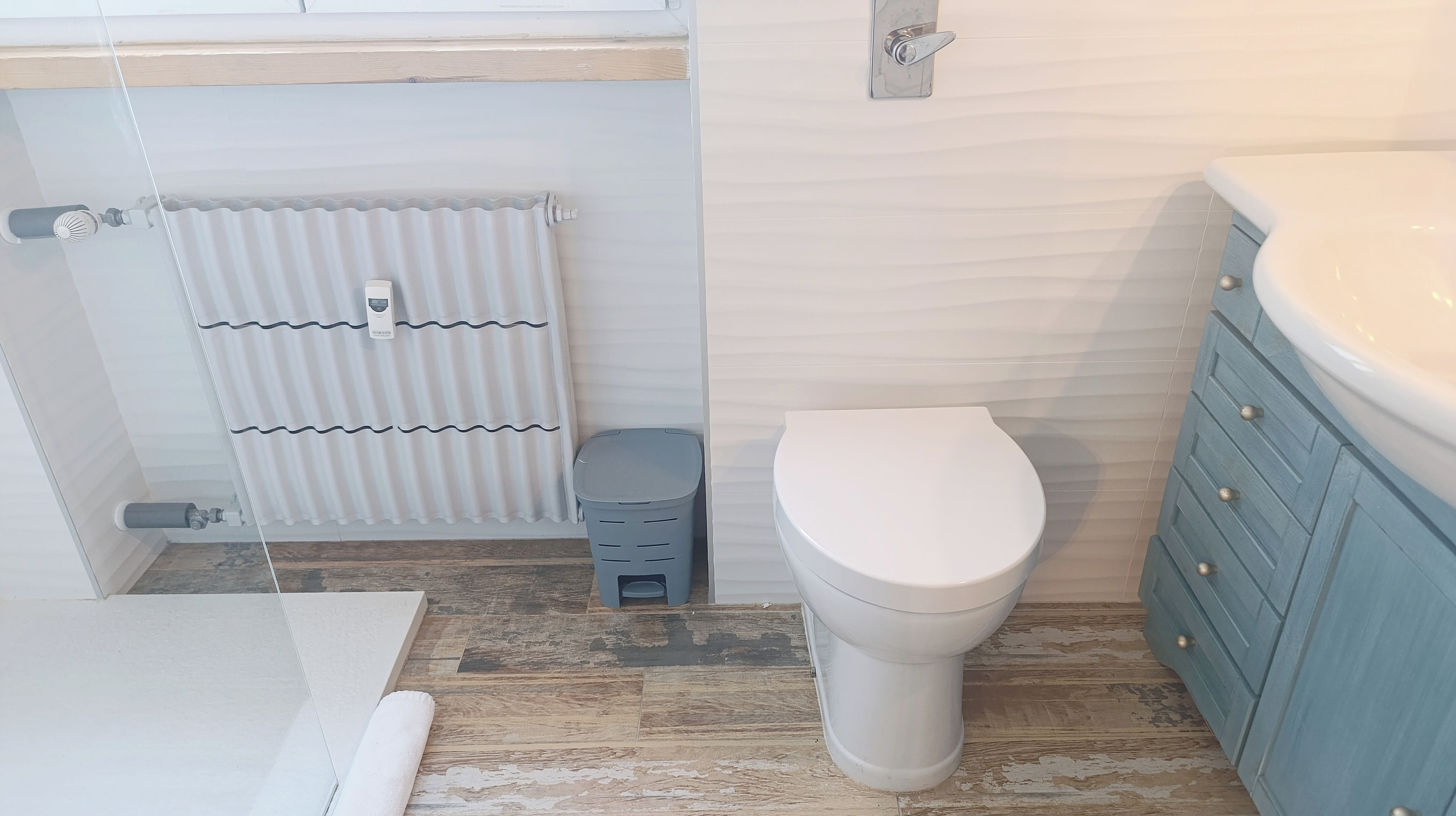 Une salle de bain comprenant des toilettes, un radiateur, une poubelle et un meuble-lavabo avec des tiroirs.