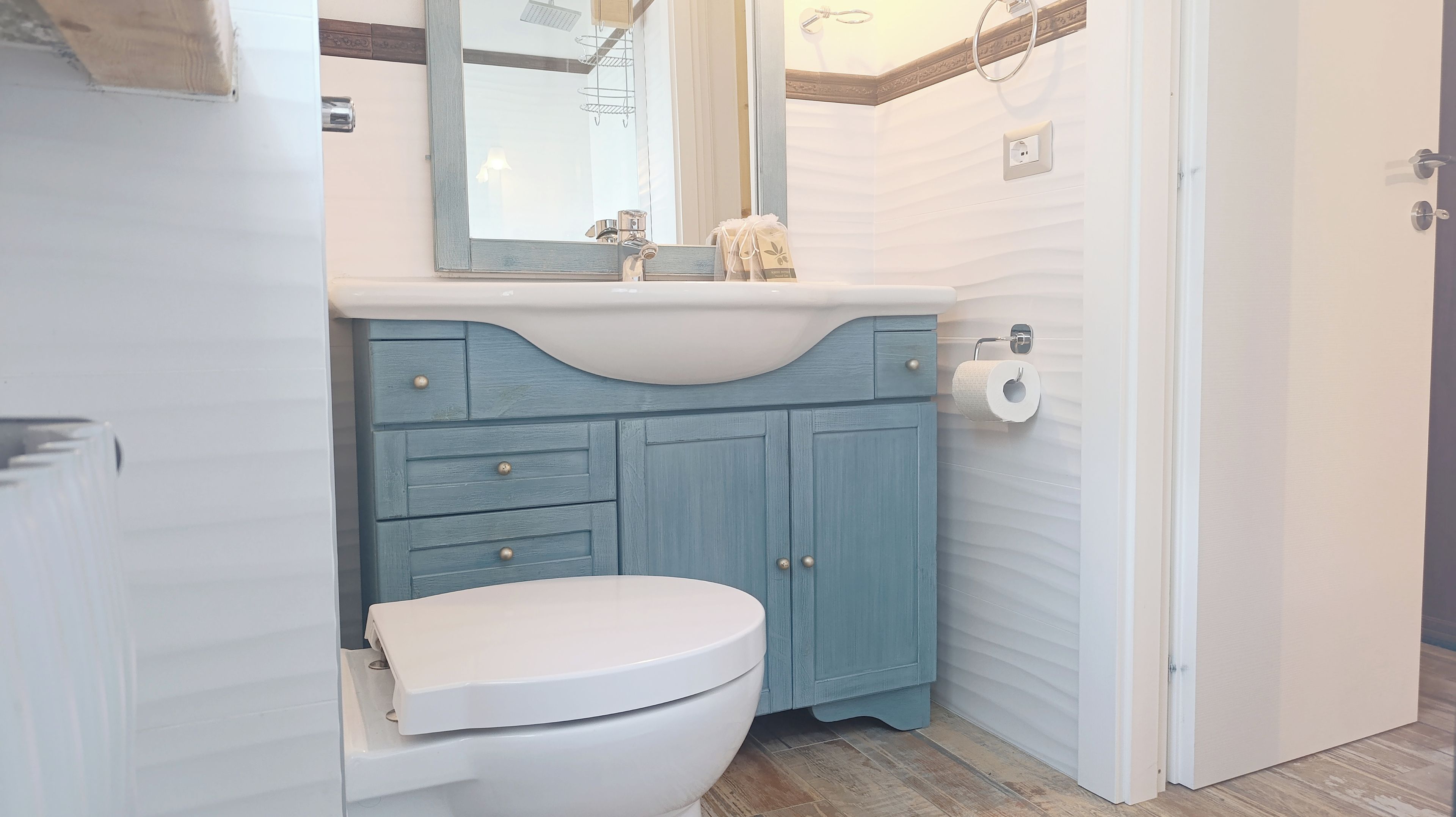 Een badkamer met een wit toilet, een blauwe wastafel met lades, een spiegel en een zeepdispenser.
