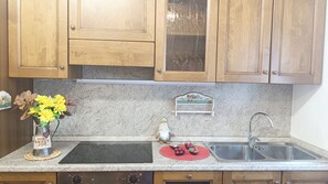 Une cuisine avec des meubles en bois, un plan de travail en granit, un évier et des objets décoratifs, notamment un vase avec des fleurs jaunes et une petite figurine.