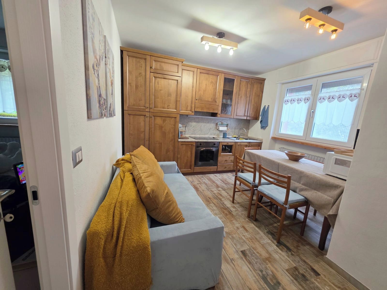 Eine kompakte Küche mit Holzausstattung, ein Essbereich mit Tisch und Stühlen sowie ein Sofa mit Decke.