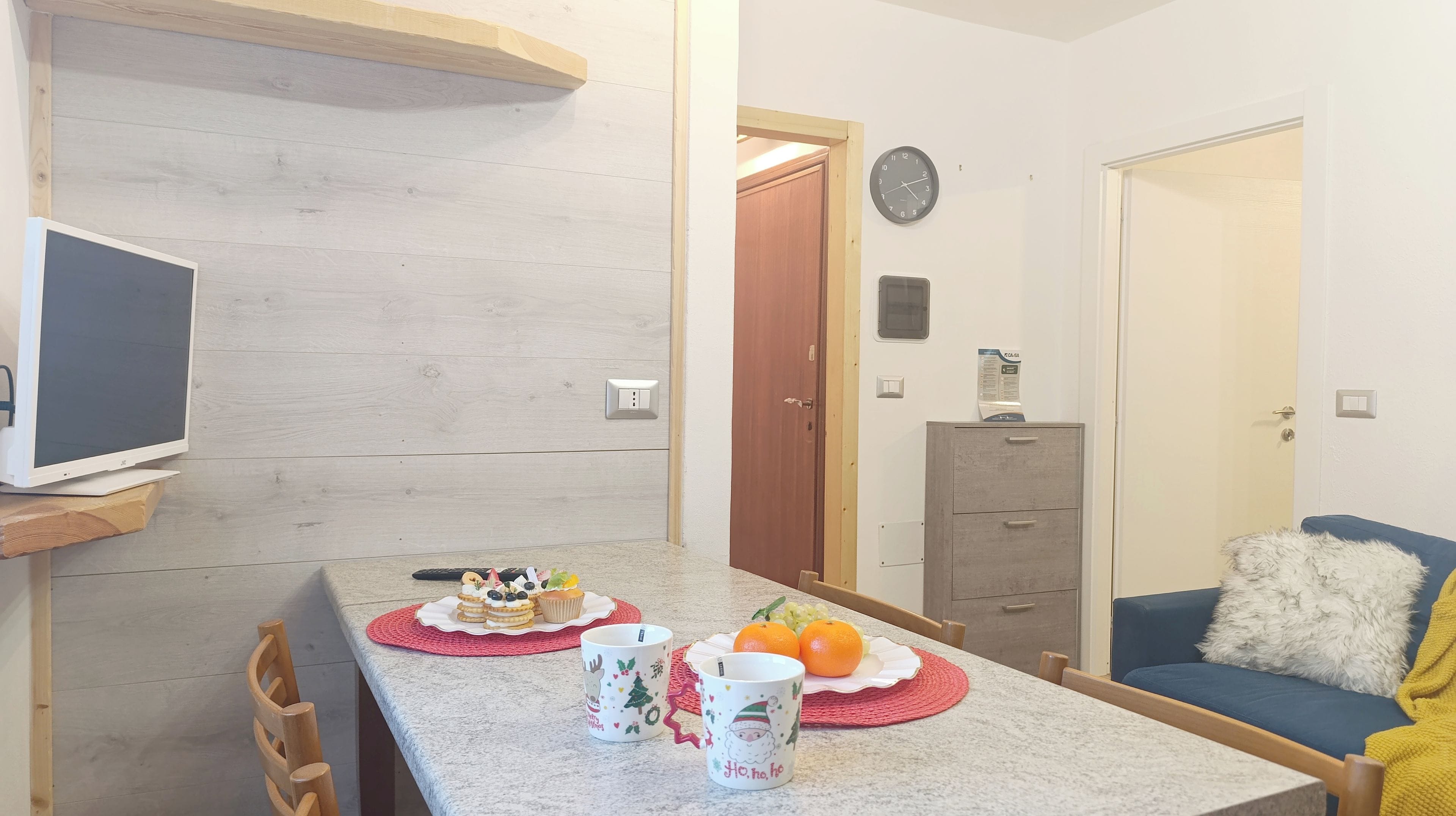 A small kitchenette with a microwave, a wooden shelf, and a dining area with a table set for two.