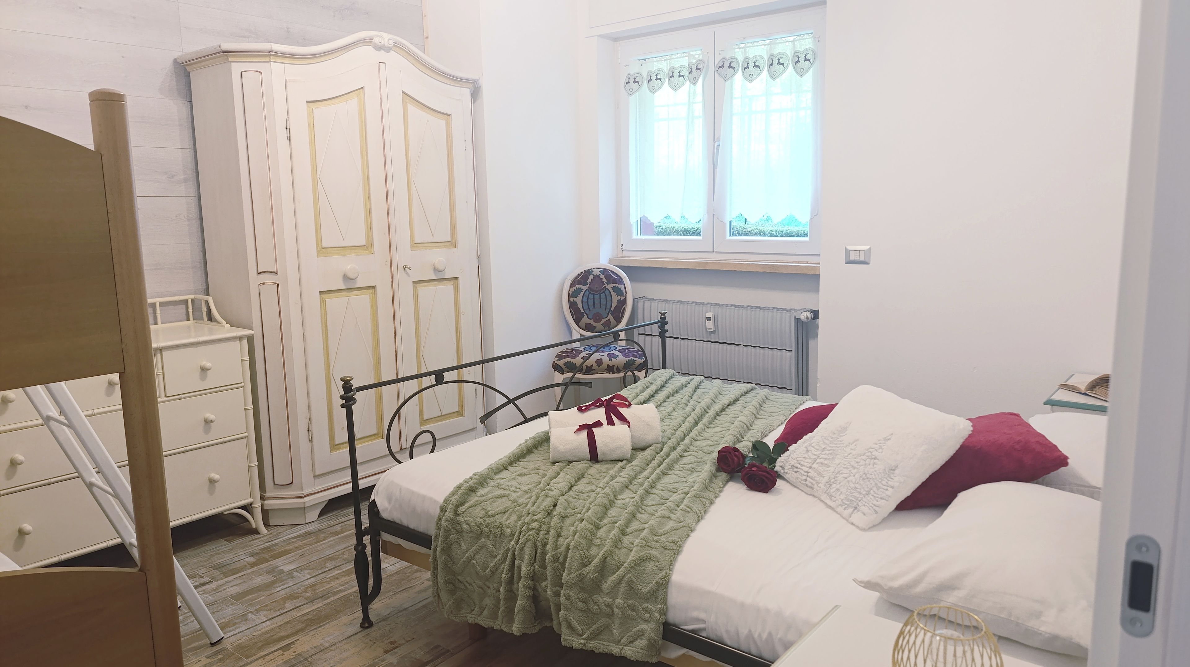 A bedroom with a bed, a wardrobe, a chair, and a window with curtains.