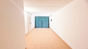 Un pasillo con una puerta cerrada al final, suelo de baldosas y paredes blancas.